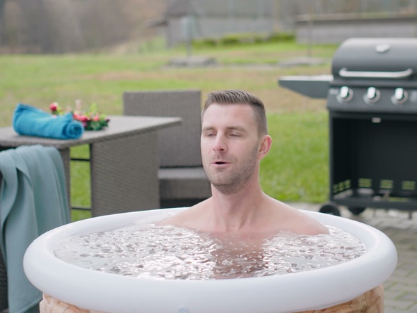 Mann sitzt im RefreshPod mit Eiswasser auf der Terrasse, dahinter Gartenmöbel und Grill